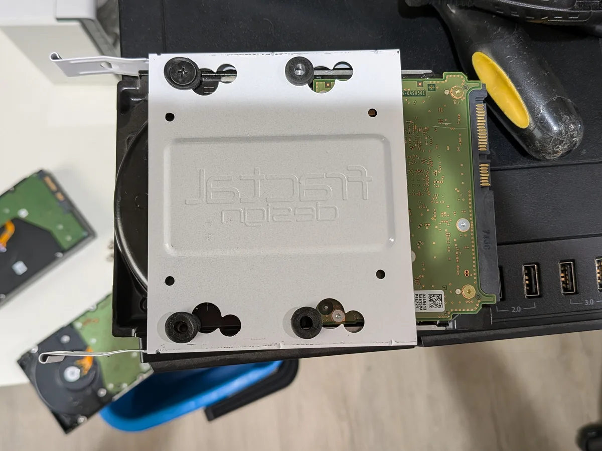 Close-up of a silver Fractal Design hard drive tray mounted on a HDD, showing green PCB and SATA connectors.