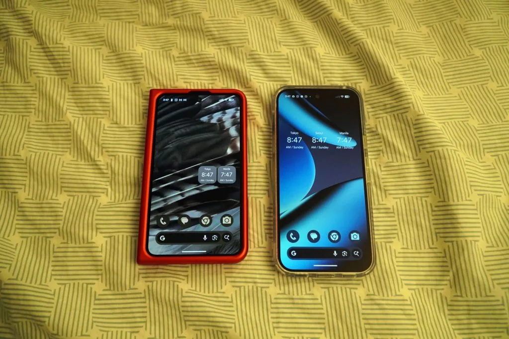 Google Pixel Fold folded in red case next to a standard smartphone on a patterned yellow fabric.