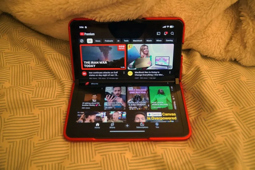 Google Pixel Fold partially folded in red case displaying YouTube app in laptop mode.